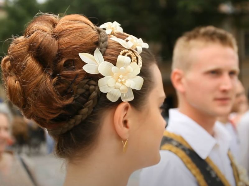 Devojka i momak u tradicionalnoj narodnoj nošnji, devojčina kosa u prvom planu, podignuta ponđa ukrašena cvetovima