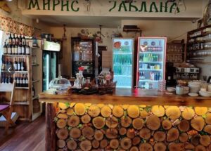 Rustični šank kafanskog restorana Miris Jablana u Beogradu sa flašama vina, frižiderima pića i dekoracijom od sečenih drvenih trupaca