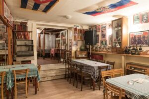 Alt tag za ovu sliku: **Unutrašnjost restorana Pavle Korčagin u Beogradu sa retro nameštajem, kariranim stolnjacima, zastavama na plafonu i zidovima prekrivenim starim fotografijama i memorabilijama**