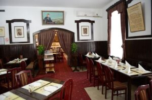Alt tag za ovu sliku: **Unutrašnjost restorana Stara Hercegovina u Beogradu sa klasičnim drvenim nameštajem, crvenim tepihom i zidovima ukrašenim slikama i portretima**
