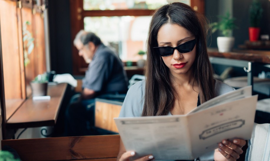 Žena sa sunčanim naočarima čita jelovnik za stolom u restoranu
